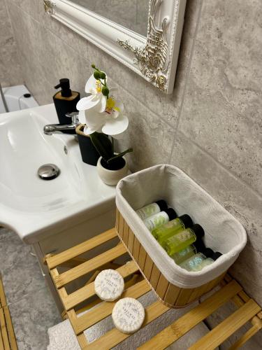 ein Waschbecken im Badezimmer mit einem Korb voller Flaschen auf einem Tisch in der Unterkunft Sofia Residence Studio Cetate in Târgu Neamţ