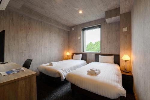 a room with two beds and a desk and a window at Mercure Niseko Resort Formerly known as Midtown Niseko in Kutchan