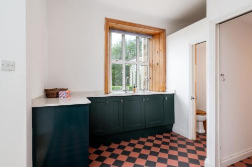 a kitchen with green cabinets and a window and a checkered floor at Finest Retreats - Walltree House in Brackley