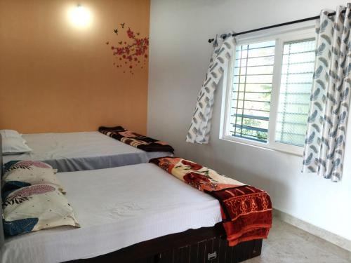two beds in a room with a window at Keshu Home Stay Hampi in Hospet