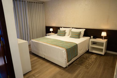 a bedroom with a white bed with two night stands and two lamps at Hz Hotel in Patos de Minas