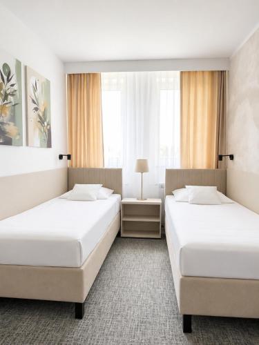 two beds in a hotel room with windows at Hotel Restauracja Kaukaska Jadwiga Choroszy in Wolsztyn