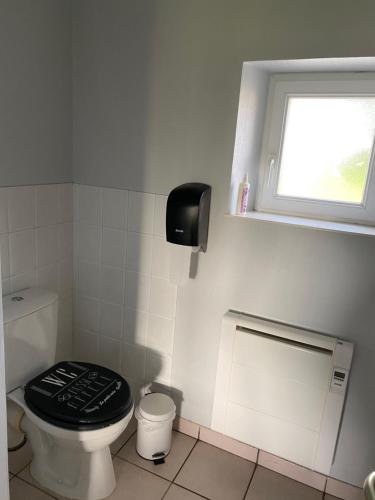 a white bathroom with a toilet with a black lid at Meublé BLEU in Réaumur