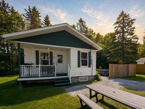 a small white cottage with a bench in the yard at WOW Chalet Boho - Charlevoix Spa Firepit and BBQ in Saint-Tite-des-Caps