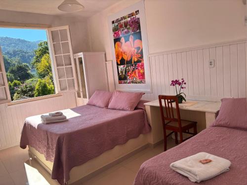 a bedroom with two beds and a desk and a window at Pousada 14 Bis in Petrópolis