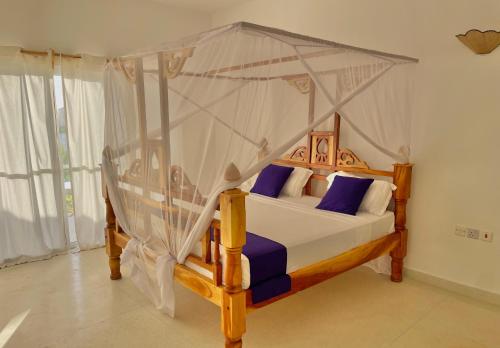 a bedroom with a canopy bed with purple pillows at Deluxe room in Watamu