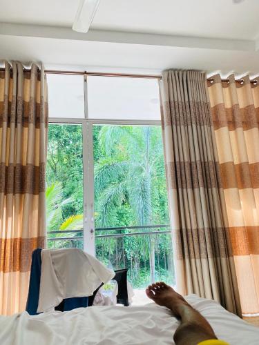 a person laying on a bed in front of a window at Reach Hotel & Restaurant in Kegalle