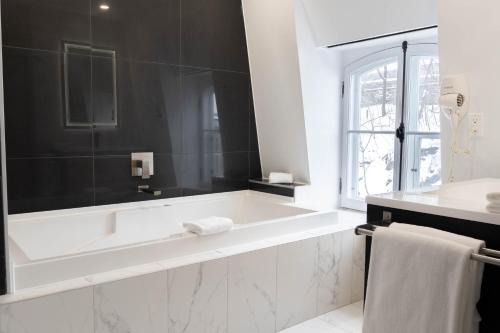 a white bathroom with a tub and a window at Hotel Le Saint-Paul in Quebec City