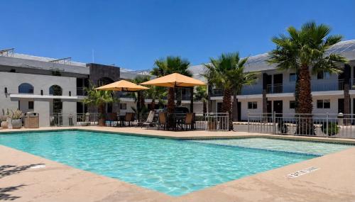 a swimming pool with chairs and umbrellas in front of a building at Hotel Villa del Sol in Ciudad Juárez