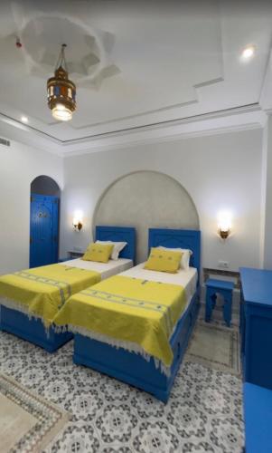 two beds in a room with blue and yellow sheets at Dar Lala Fatma in Le Lido