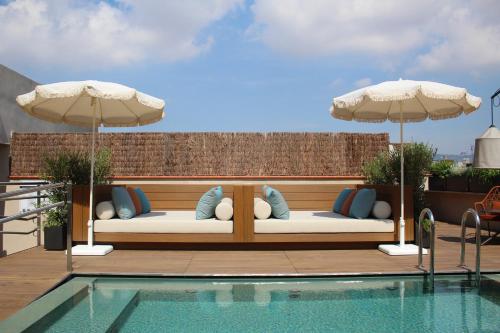 ein Pool mit einer Bank mit Kissen und Sonnenschirmen in der Unterkunft Hotel Medinaceli 4 Sup in Barcelona