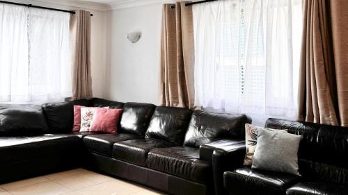a black leather couch in a living room with windows at The Perch - Lifestyle Yamba in Yamba