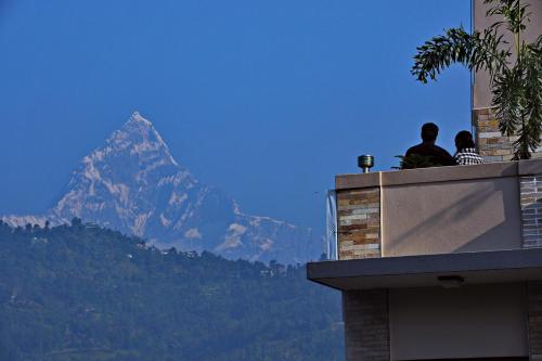 two people sitting on a ledge looking at a mountain at Hotel Queens Park in Pokhara