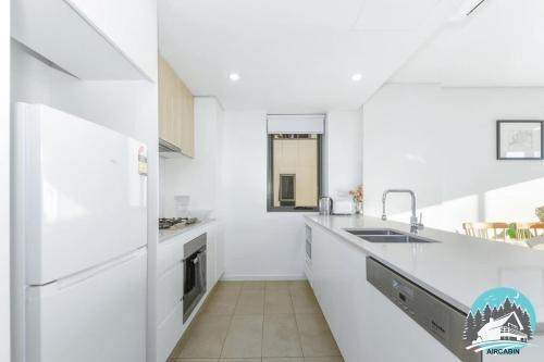 a white kitchen with a sink and a refrigerator at Asquith 2BR Apt Secure Underground Parking in Asquith