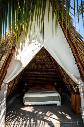 a bed in a thatched tent under a palm tree at Tribu Hostal in El Paredón Buena Vista