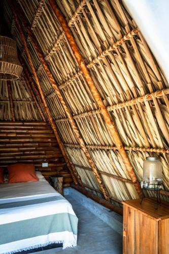 a bedroom with a bed in a thatched room at Tribu Hostal in El Paredón Buena Vista