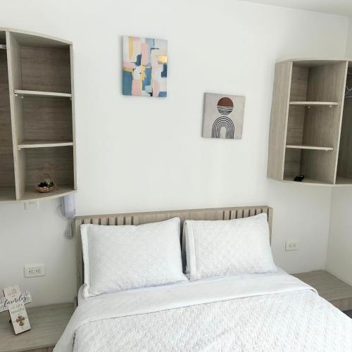 a bedroom with a bed with white sheets and shelves at Hotel Zona Oro in Armenia