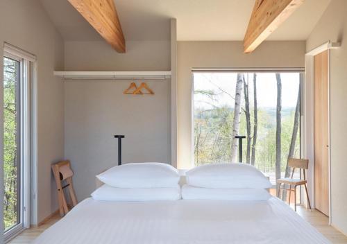 a bedroom with a white bed and a large window at Adagio Retreat Tokachidake in Biei