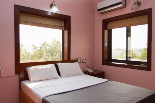 a bedroom with pink walls and a bed with two windows at Westwood Residence Goa - The Boutique Hotel in Mapusa