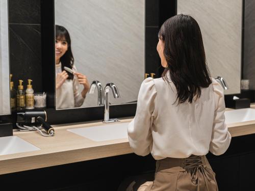 a woman standing in front of a bathroom mirror at TsukubaNoYu Urban Hotel in Tsukuba