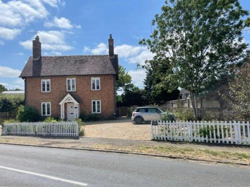 a large brick house with a white picket fence at Elm Cottage in Alvescot