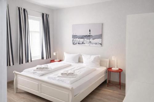 a white bedroom with a large white bed with two lamps at Ille in Wittdün
