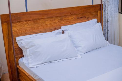 a bed with white pillows and a wooden headboard at CAM Apartments in Dodoma