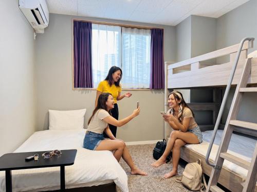 a group of three girls sitting in a room with bunk beds at BANDE Hotel in Namba in Osaka