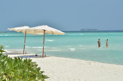 a beach with an umbrella and two people in the water at Olhumathi View Inn in Ukulhas
