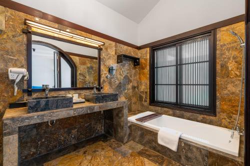 a bathroom with a tub and a sink and a mirror at RMH Le Belhamy Beach Resort in Hoi An