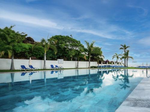 a swimming pool with blue chairs and palm trees at Hotel Las Águilas Tenerife, Affiliated by Meliá in Puerto de la Cruz