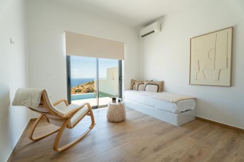 a bedroom with a bed and a chair and a window at Serenity Villas in Ios Chora