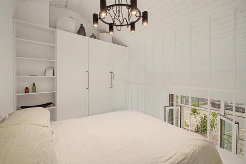 a white bedroom with a bed and a chandelier at The Village Barn in Caniço