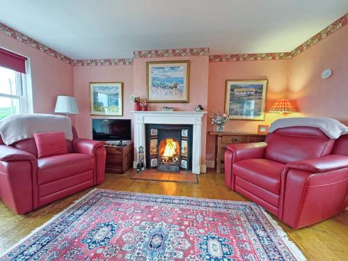 a living room with two red chairs and a fireplace at Vindolanda in Fearnmore