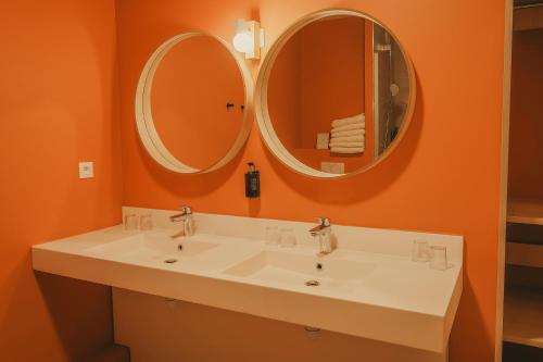 a bathroom with two sinks and two mirrors at Hôtel Le Refuge des Sources in Digne-les-Bains