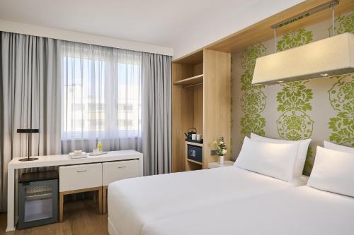 a bedroom with a bed and a desk and a window at NH Berlin Potsdamer Platz in Berlin