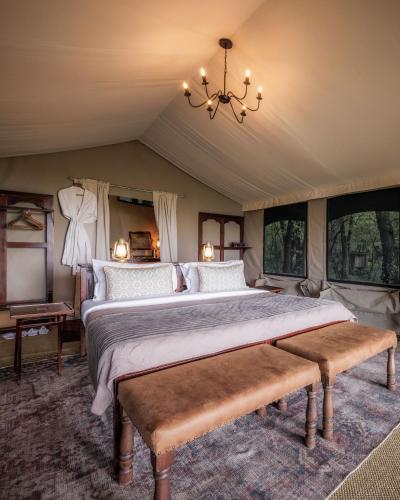 a bedroom with a large bed with a chandelier and windows at Elephant Pepper Camp in Masai Mara