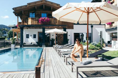 a man sitting on lounge chairs next to a swimming pool at Boutique Hotel Das Rivus in Leogang