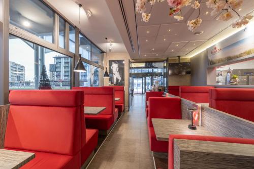 a restaurant with red chairs and tables and windows at Ramada The Hague Scheveningen in Scheveningen