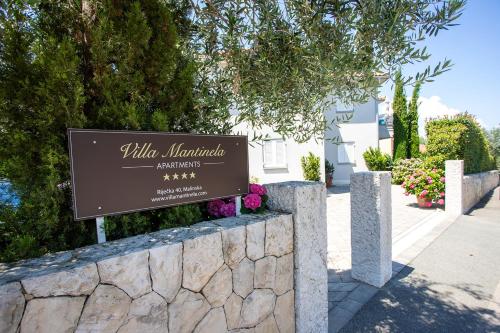 a sign for a villa with flowers on a stone wall at Apartments Villa Mantinela in Malinska