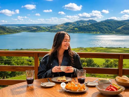 a woman sitting at a table with a bowl of food at Chalés da Lagoa - Imaruí/SC in Imaruí