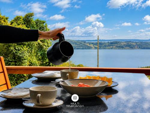 a person holding a pot over a table with a bowl of food at Chalés da Lagoa - Imaruí/SC in Imaruí