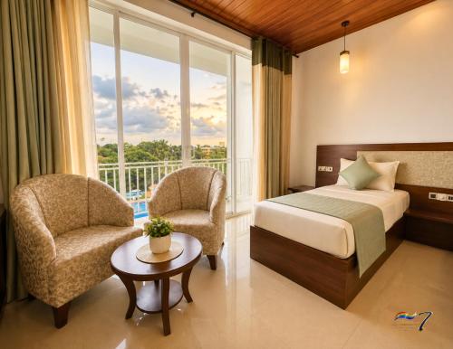a hotel room with a bed and chairs and a window at Rainbow Seven Hotel in Negombo