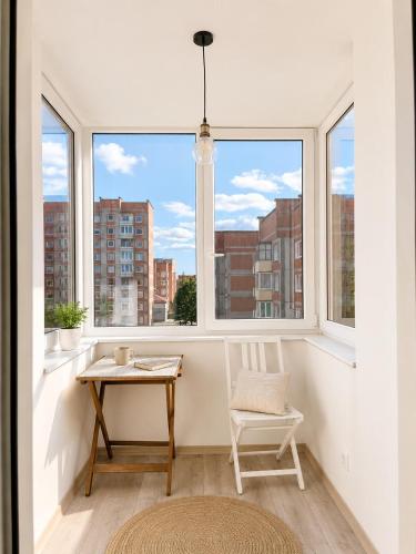 a table and a chair in a room with windows at Mis apartamentai in Mažeikiai