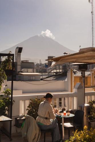 a woman sitting at a table on a balcony with a mountain at Maison verte - Guest House in Arequipa