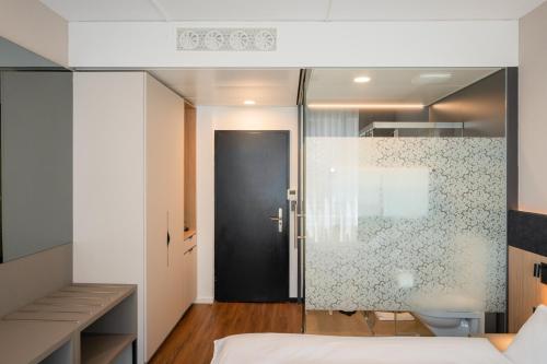 a bedroom with a glass door leading to a bathroom at Tailormade Hotel METROPOL St Gallen in St. Gallen