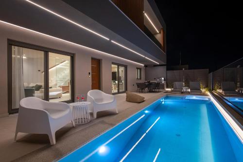 a swimming pool in a house with white chairs at Villa Nectar in Kounoupidhianá