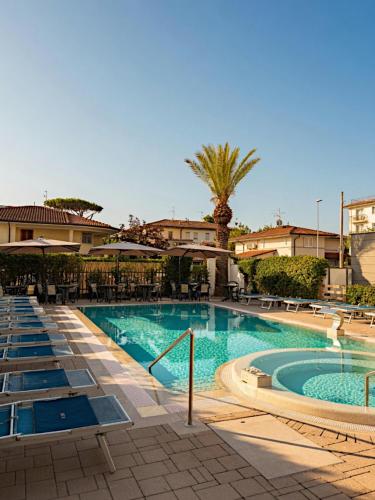 a swimming pool with chairs and a palm tree at Hotel Fortunella in Lido di Camaiore