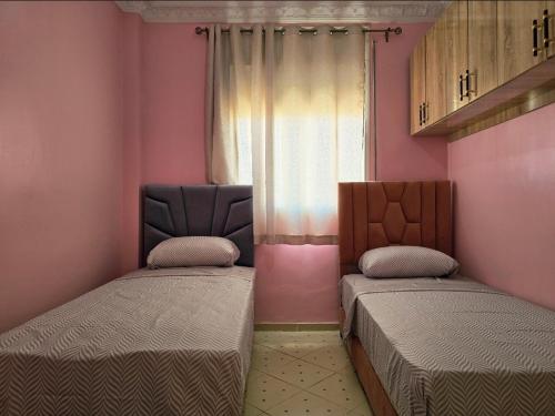 two beds in a room with pink walls and a window at Morjan apart in Tangier