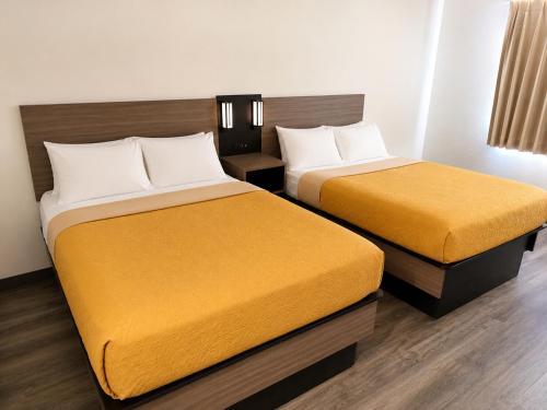 two beds in a hotel room with yellow sheets at Dickinson Inn in Dickinson
